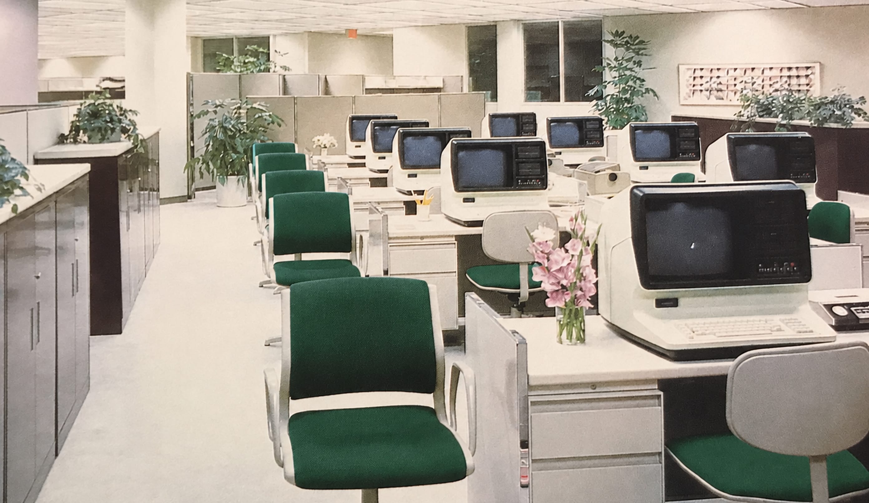 Rows of computer terminals and green chairs in a sunlit office.